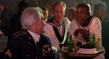 Movie still from “Dirty Rotten Scoundrels” (1988), directed by Frank Oz – A group of men sitting at a table with a beer; Medium shot, Over the shoulder angle