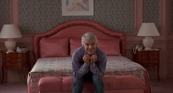 Movie still from “Dirty Rotten Scoundrels” (1988), directed by Frank Oz – A man sitting on the edge of a bed in front of a painting on the wall; Medium shot, High angle