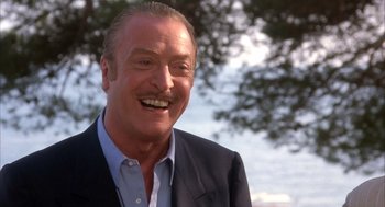 Movie still from “Dirty Rotten Scoundrels” (1988), directed by Frank Oz – An older man smiling for the camera with trees in the background; Close Up shot, Low angle