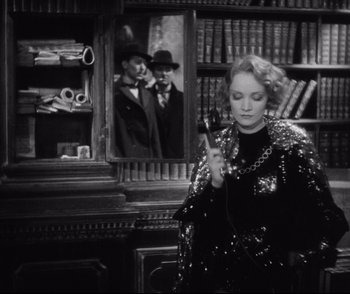 Movie still from “Dishonored” (1931), directed by Josef von Sternberg – A woman holding a microphone in front of a picture of a man; Medium shot, Low angle