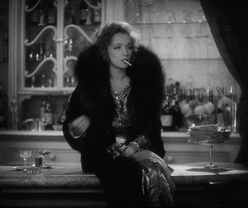 Movie still from “Dishonored” (1931), directed by Josef von Sternberg – An older woman smoking a cigarette while sitting on a bar; Medium shot, Low angle