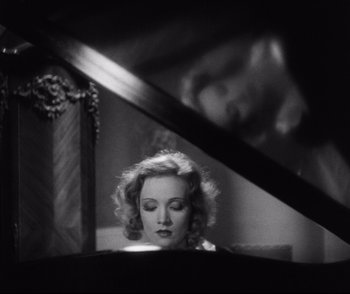 Movie still from “Dishonored” (1931), directed by Josef von Sternberg – A black and white photo of a woman sitting at a piano; Close Up shot, High angle