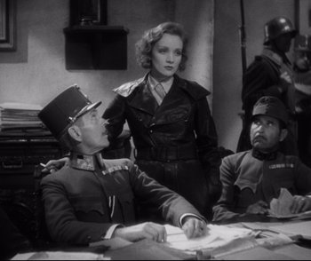 Movie still from “Dishonored” (1931), directed by Josef von Sternberg – A man and a woman in military garb sit at a table with another man; Medium shot, Over the shoulder angle