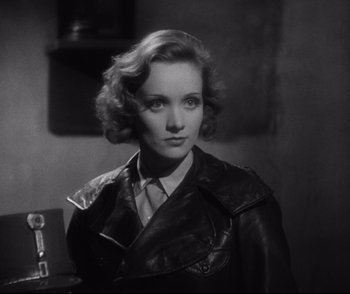 Movie still from “Dishonored” (1931), directed by Josef von Sternberg – A black and white photo of a woman in a leather jacket; Close Up shot, Over the shoulder angle