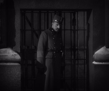 Movie still from “Dishonored” (1931), directed by Josef von Sternberg – A man in a uniform standing in front of a jail cell; Medium shot, Low angle