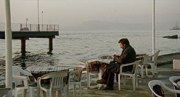 Movie still from “Distant” (2002), directed by Nuri Bilge Ceylan – A man sitting at a table by the water; Wide shot, High angle