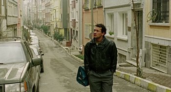 Movie still from “Distant” (2002), directed by Nuri Bilge Ceylan – A man standing on the side of the street holding a bag; Wide shot, Low angle