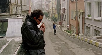 Movie still from “Distant” (2002), directed by Nuri Bilge Ceylan – A man is eating something while walking down the street; Wide shot, Low angle