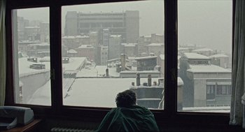 Movie still from “Distant” (2002), directed by Nuri Bilge Ceylan – A person looking out of a window at a snowy city; Extreme Wide shot, High angle