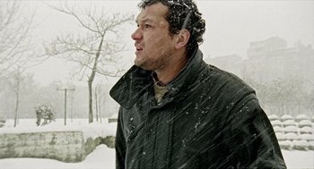 Movie still from “Distant” (2002), directed by Nuri Bilge Ceylan – A man standing in the snow with a tree in the background; Medium shot, Low angle