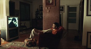 Movie still from “Distant” (2002), directed by Nuri Bilge Ceylan – A man sitting in a chair in a living room; Wide shot, High angle