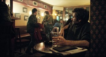 Movie still from “Distant” (2002), directed by Nuri Bilge Ceylan – A man sitting at a table holding a glass of wine; Medium shot, Over the shoulder angle