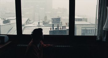 Movie still from “Distant” (2002), directed by Nuri Bilge Ceylan – A man sitting in front of a window looking out on a snowy day; Wide shot, High angle