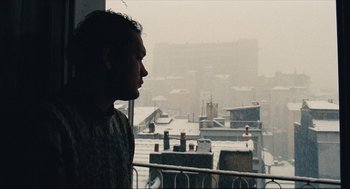 Movie still from “Distant” (2002), directed by Nuri Bilge Ceylan – A man looking out of a window at a snowy city skyline; Medium shot, Low angle