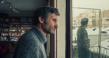 Movie still from “Distant” (2002), directed by Nuri Bilge Ceylan – A man standing in front of a window looking outside; Medium shot, Over the shoulder angle