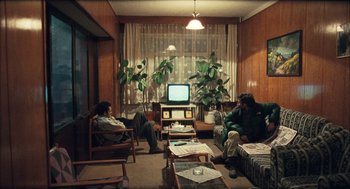 Movie still from “Distant” (2002), directed by Nuri Bilge Ceylan – Two people sitting in front of a television in a living room; Wide shot, High angle
