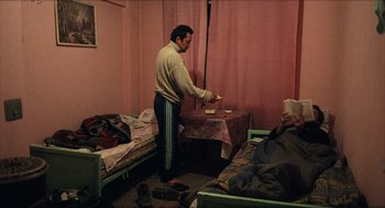 Movie still from “Distant” (2002), directed by Nuri Bilge Ceylan – A man standing in front of a table in a room; Wide shot, High angle