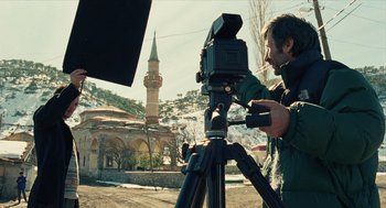 Movie still from “Distant” (2002), directed by Nuri Bilge Ceylan – A man with a camera on a tripod in front of a building; Medium shot, Low angle