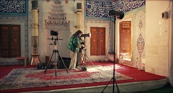 Movie still from “Distant” (2002), directed by Nuri Bilge Ceylan – A man standing in front of a camera in a room; Wide shot, High angle