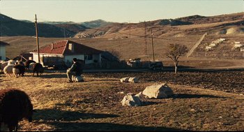 Movie still from “Distant” (2002), directed by Nuri Bilge Ceylan – A man sitting on top of a field next to a house; Extreme Wide shot, High angle