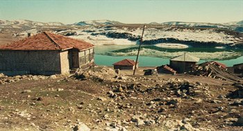 Movie still from “Distant” (2002), directed by Nuri Bilge Ceylan – An old house sits on the side of a lake; Extreme Wide shot, High angle