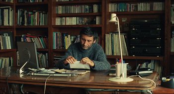 Movie still from “Distant” (2002), directed by Nuri Bilge Ceylan – A man sitting at a desk in front of a book case; Medium shot, Over the shoulder angle