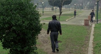 Movie still from “Distant” (2002), directed by Nuri Bilge Ceylan – A man walking in a park while a woman walks by; Wide shot, High angle
