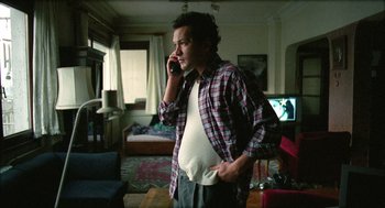 Movie still from “Distant” (2002), directed by Nuri Bilge Ceylan – A man talking on a cell phone while standing in a living room; Medium shot, Low angle