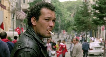 Movie still from “Distant” (2002), directed by Nuri Bilge Ceylan – A man smoking a cigarette while standing in a crowd of onlookers; Close Up shot, Low angle