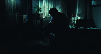 Movie still from “Distant” (2002), directed by Nuri Bilge Ceylan – A person sitting in a dark room at night; Wide shot, Low angle