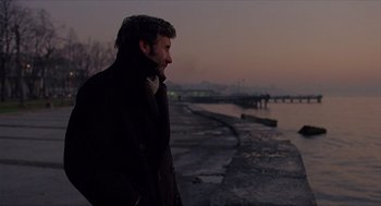 Movie still from “Distant” (2002), directed by Nuri Bilge Ceylan – A man standing next to a body of water at dusk; Medium shot, Low angle