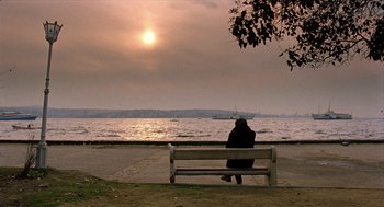Movie still from “Distant” (2002), directed by Nuri Bilge Ceylan – A person sitting on a bench looking out at the water; Extreme Wide shot, High angle