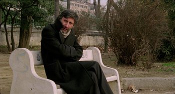 Movie still from “Distant” (2002), directed by Nuri Bilge Ceylan – A man sitting on top of a white bench in a park; Medium shot, Low angle