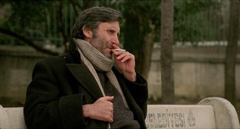 Movie still from “Distant” (2002), directed by Nuri Bilge Ceylan – A man sitting on top of a bench eating something; Medium shot, Low angle