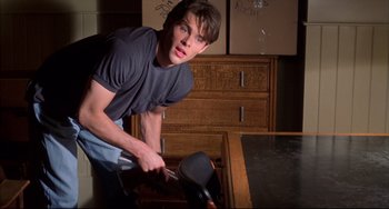 Movie still from “Disturbing Behavior” (1998), directed by David Nutter – A young man holding a hammer in a room with wooden furniture; Medium shot, High angle
