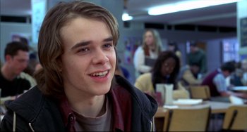 Movie still from “Disturbing Behavior” (1998), directed by David Nutter – A young man smiling for the camera in front of a group of people; Close Up shot, Over the shoulder angle