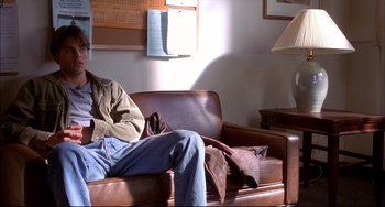 Movie still from “Disturbing Behavior” (1998), directed by David Nutter – A man sitting on a brown leather couch in a living room; Medium shot, High angle