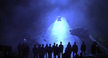Movie still from “Disturbing Behavior” (1998), directed by David Nutter – A group of people standing on the side of a road at night; Extreme Wide shot, High angle