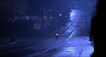 Movie still from “Disturbing Behavior” (1998), directed by David Nutter – A person riding a motorcycle down a street at night; Extreme Wide shot, High angle