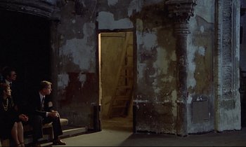 Movie still from “Diva” (1981), directed by Jean-Jacques Beineix – A man sitting on steps in front of an open door; Wide shot, High angle