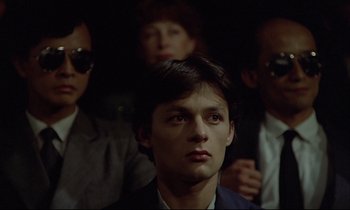 Movie still from “Diva” (1981), directed by Jean-Jacques Beineix – A man in a suit is looking at the camera; Close Up shot, Over the shoulder angle