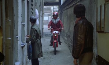 Movie still from “Diva” (1981), directed by Jean-Jacques Beineix – A man riding a motorcycle down a narrow alley way; Wide shot, Over the shoulder angle