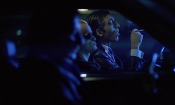 Movie still from “Diva” (1981), directed by Jean-Jacques Beineix – A man sitting in the back seat of a car while smoking a cigarette; Medium shot, Over the shoulder angle