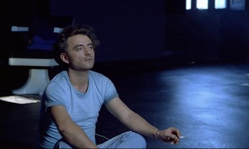Movie still from “Diva” (1981), directed by Jean-Jacques Beineix – A man sitting on the ground holding a cell phone; Close Up shot, Low angle