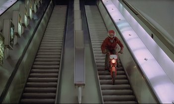 Movie still from “Diva” (1981), directed by Jean-Jacques Beineix – A man riding a motorcycle down an escalator; Wide shot, Low angle
