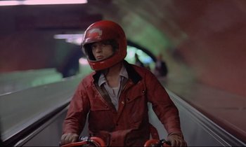 Movie still from “Diva” (1981), directed by Jean-Jacques Beineix – A man riding a bike down the side of an escalator; Medium shot, High angle