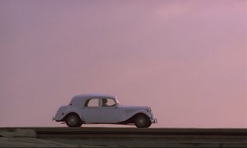 Movie still from “Diva” (1981), directed by Jean-Jacques Beineix – An old car is driving down the road; Extreme Wide shot, Low angle