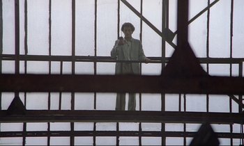 Movie still from “Diva” (1981), directed by Jean-Jacques Beineix – A man in a suit and tie standing in front of a window; Wide shot, Low angle