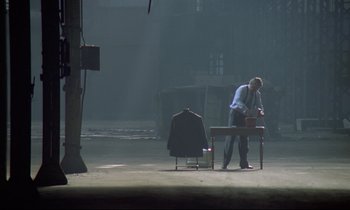 Movie still from “Diva” (1981), directed by Jean-Jacques Beineix – A man sitting on a bench in the middle of an empty room; Wide shot, High angle