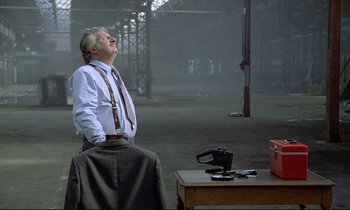 Movie still from “Diva” (1981), directed by Jean-Jacques Beineix – A man in a suit and tie standing next to a table; Wide shot, Low angle